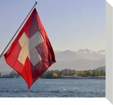 Drapeau suisse flottant sur un lac avec montagnes en arrière-plan.